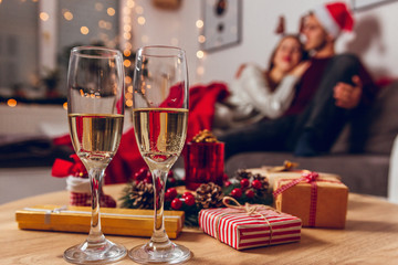 Merry Christmas and Happy New Year! Romantic couple enjoying and cuddling for Christmas at home. 
Focus on table with champagne and gifts.