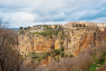 A view to El Tajo Gorge Canyon, traditional andalusian houses at the cliff and a lot of almond trees on the slope at famous white village Ronda in Malaga province, Andalusia, Spain.