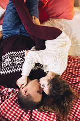 Happy couple dressed in the sweaters is kissing and hugging near the christmas tree, cozy atmosphere and love, home and family, white caucasian couple