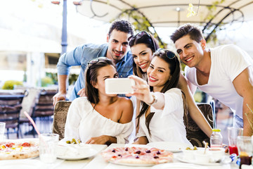Group of young beautiful people sitting in a restaurant and taki
