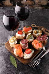 Italian antipasti wine snacks set. Cheese variety, Mediterranean olives, pickles, salami, salmon, tomatoes, artichokes and wine in glasses. Spanish tapas