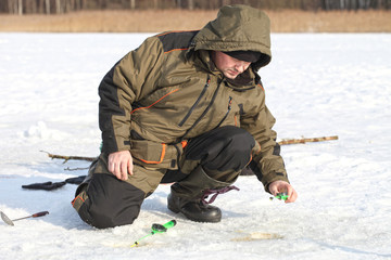 The fisherman catches fish in the winter from the hole. Ice fishing on a sunny day.