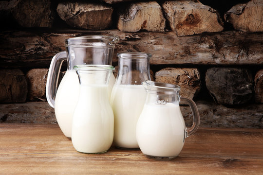 A jug of milk and glass of milk on a wooden table.