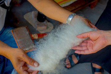 Close up of a man holding in his hand a piece of wool to work on loom manufacturing whool shawl...
