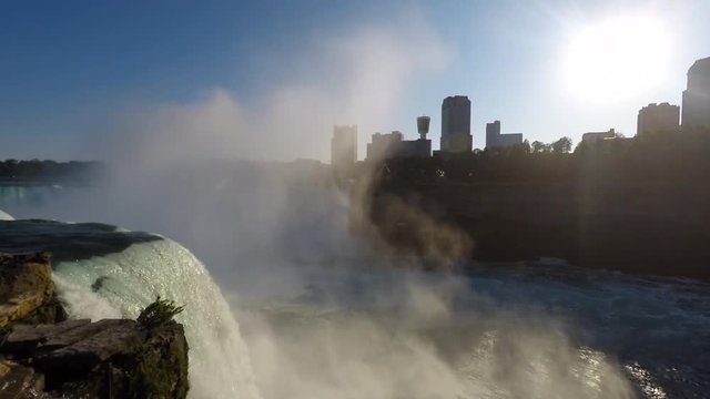 Niagara Falls State Park of New York USA with roaring mist rising over American Falls, skyline of Niagara Falls City Canada in background with setting sun