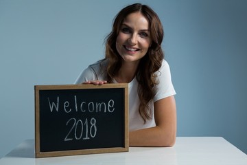 Smiling woman showing slate with text welcome 2018 against grey