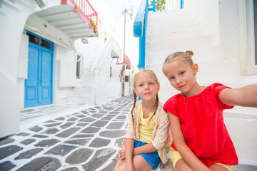 Two little girls taking selfie photo outdoors in greek village on narrow street in Mykonos