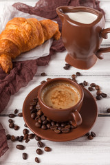 Freshly baked croissants on brown napkin, cream, to cups of coffee in ceramic dishes on white wooden background. Fresh pastries for breakfast. Delicious dessert. Closeup photography. Vertical banner