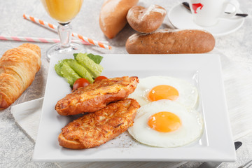 Bread fried in cheese served with fried eggs, lettuce and tomato. Breakfast conception with fresh orange juice, coffee and croissant