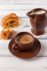 Freshly baked croissants on brown napkin, cream, to cups of coffee in ceramic dishes on white wooden background. Fresh pastries for breakfast. Delicious dessert. Closeup photography. Vertical banner