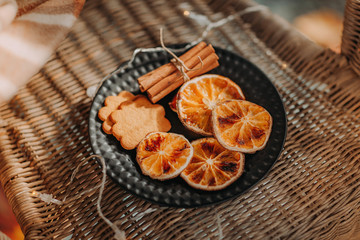 dried slices of oranges, gingerbread cookies and cinnamon sticks on black plate