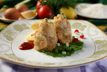 Catfish fillet in batter.On the plate with lemon wedges and vegetables.