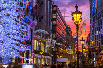 Budapest, Hungary - Glowing Christmas tree and tourists on the busy Vaci street, the famous shopping street of Budapest at Christmas time with shops and beautiful sunset sky