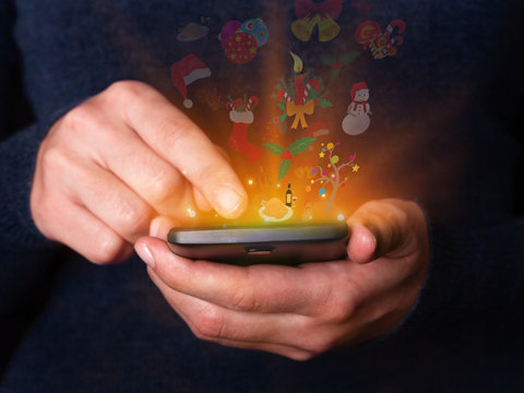 Woman hands holding and using smartphone mobile or cell phone for Christmas or xmas. Concept for celebration with logos of  Santa Claus hat, holy berry, snowman, gingerbread, candle, bells and turkey.
