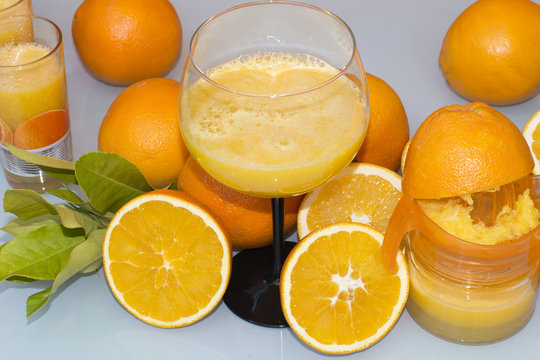 Una copa con zumo de naranja, naranjas sobre la mesa, un exprimidor manual 