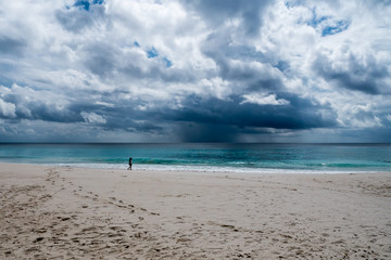 woman walking alone on a tropical beach while a storm is coming