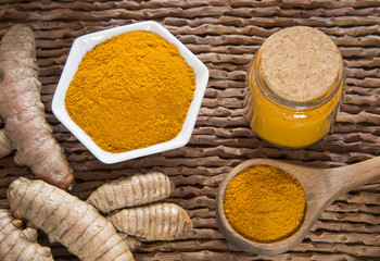 Turmeric powder and fresh turmeric on wooden background