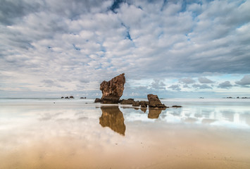 summer afternoon at the Aguilar beach, Asturias, where the monolith plays with the reflected clouds and the sea