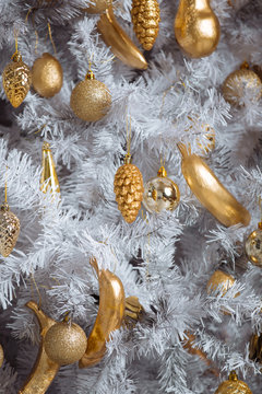 Golden christmas toys hanging on white artificial christmas tree