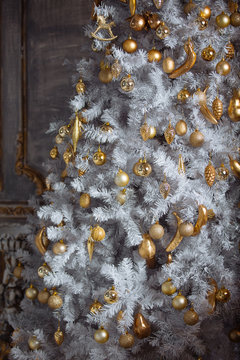 Golden christmas toys hanging on white artificial christmas tree