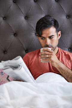 Millennial Man Having Coffee And Reading The Paper In Bed