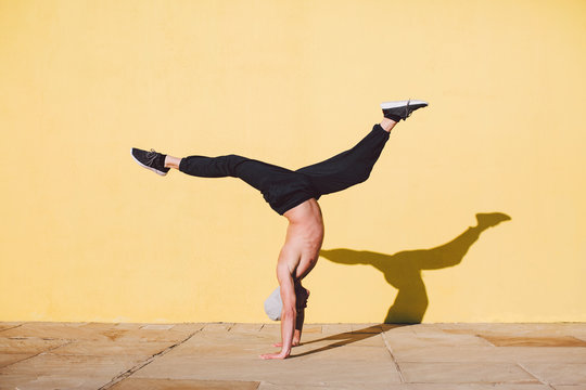 Man breakdancing in front of a yellow wall.
