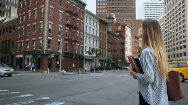 Young beautiful businesswoman holding the documents and crossing the road in financial district of New York. Slow motion
