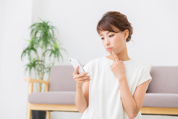 部屋でスマホを見る女性　考える