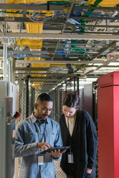 Two server room techs beneath a ceiling of network cables