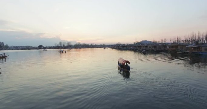 Aerial, people paddle boats on Jhelum River at sunset