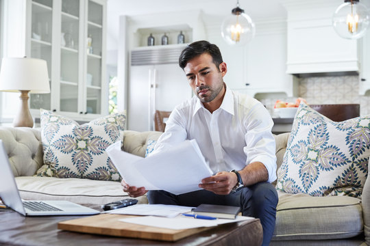 Hispanic Businessman Reading Contracts At Home In Living Room