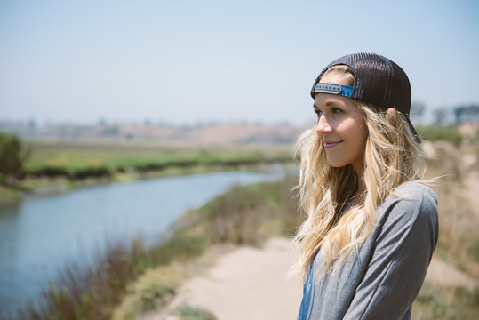 Woman with backwards cap stands along a stream