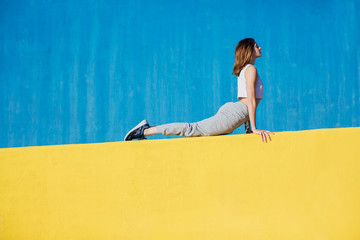 Young ginger woman doing yoga exercises in front of a colorful wall.