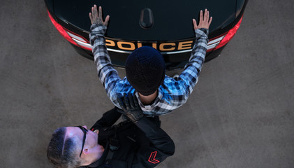 A suspect is searched by a Police Officer at the rear of his cruiser
