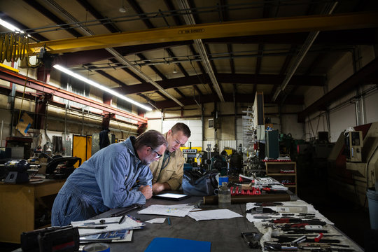Two male factory workers leaning over digital tablet