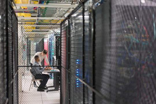 Two server room technicians in a security cage talk at a desk