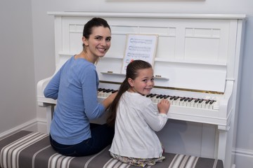 Portrait of mother assisting daughter in playing piano