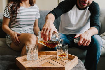 A man and woman sitting on the couch. Pour scotch / whiskey on glasses