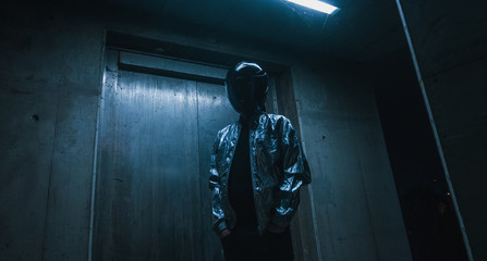 Futuristic scene with person with black helmet/mask and silver jacket with neons iluminating around.