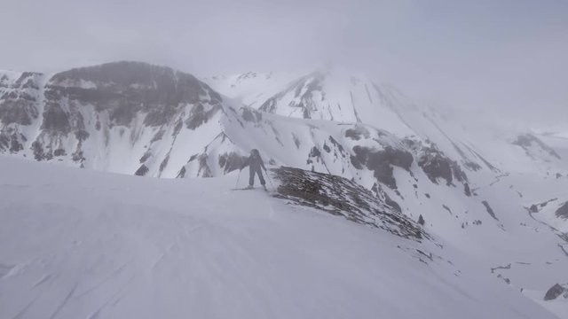 Aerial, skier prepares to descend down mountain slope