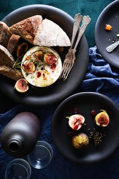 Baked Camembert cheese and fruits on plates on a table seen from overhead.