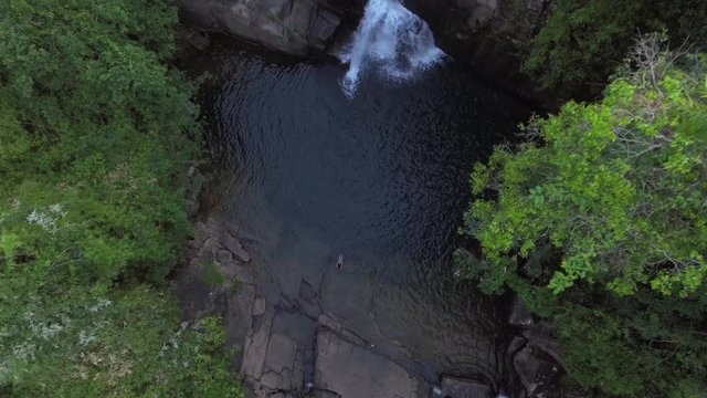 aerial shot woman swimming alone in waterfall pond in a forest