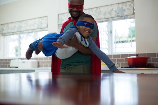 Son and father pretending to be a superhero in kitchen