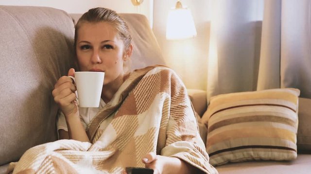 Young female is watching TV and sitting with tea at home.