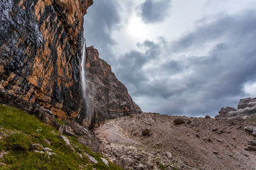 Waterfall at the foots of vertical and majestic western side of Tofana di Rozes Peak, Travenanzes Valley, Dolomites, Italy