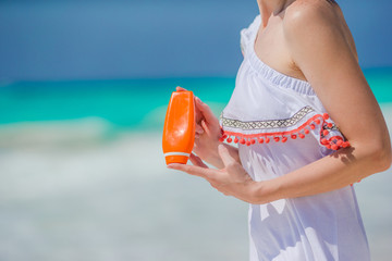 Suncream bottle in female hands on the beach.