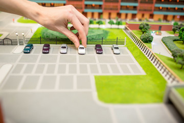 Human hand taking one of car models from parking place on layout of modern city