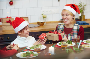 Happy senior female and her grandsone exchanging by giftboxes by Christmas dinner