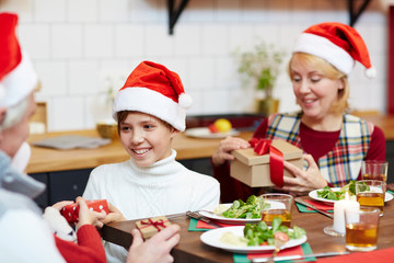 Cute boy giving small package to his sister by festive dinner with grandparents