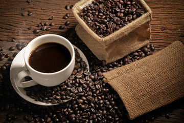 warm cup of coffee with sack inside by coffee bean on wood background